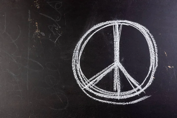 Close up of white chalk peace sign on black chalkboard background. Peace and anti war movement concept.