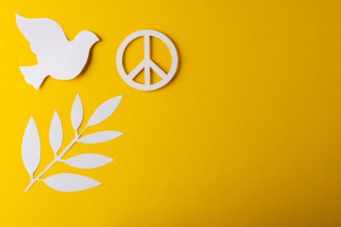 Beyaz barış işaretinin yüksek açılı görüntüsü, beyaz güvercin ve sarı arka planda kopya alanı olan yaprak. Barış ve savaş karşıtı hareket kavramı.