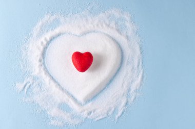 Kırmızı kalp, mavi arka planda kalp şeklinde şekerin üstünde. Diyet, kan şekeri, diyabet ve kalp sağlığı farkındalığı.