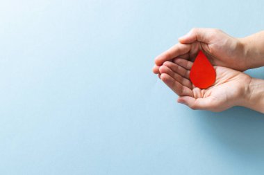 Kafkas kadının elleri, mavi arka planda kan damlalarını kopyalanmış şekilde tutuyor. Kan bağışı, ilaç ve sağlık hizmetleri.