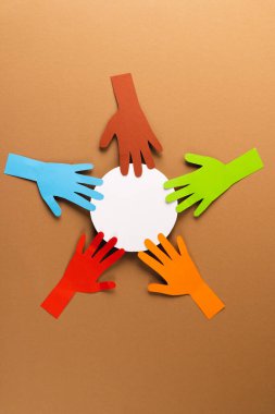 Kağıt, çok renkli ellerden ve beyaz çemberden kesilmiş. Kahverengi zemin üzerinde kopyalama alanı var. İnsani yardım, insanlar, yardım ve insan kavramı.