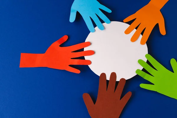 stock image Paper cut out of multi coloured hands and white circle with copy space on blue background. Humanitarian, people, help and human concept.