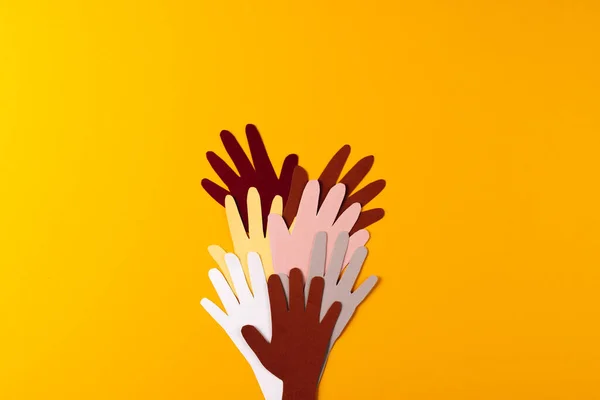 Paper cut out of multi coloured hands with copy space on orange background. Humanitarian aid, people, help and human concept.
