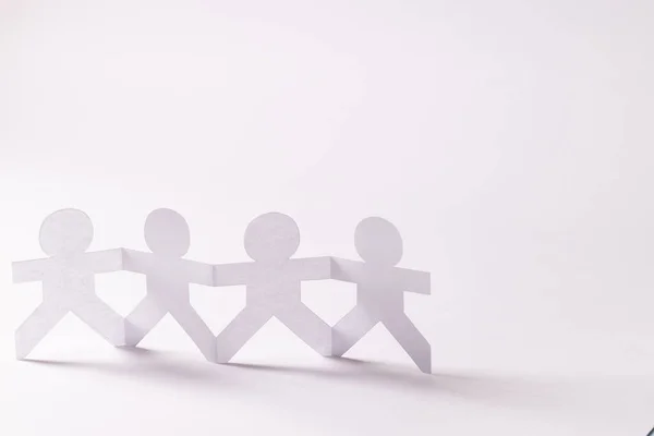 Close up of four paper cut out people figures holding hands with copy space on white background. Humanitarian, people, help and human concept.