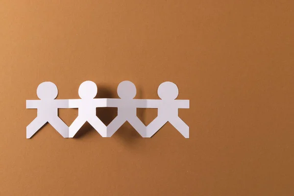 Close up of four paper cut out people figures holding hands with copy space on brown background. Humanitarian, people, help and human concept.