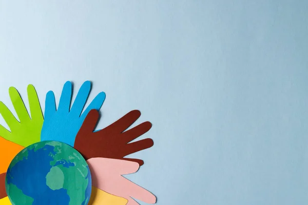 Paper cut out of multi coloured hands and globe with copy space on blue background. Humanitarian aid, people, help and human concept.