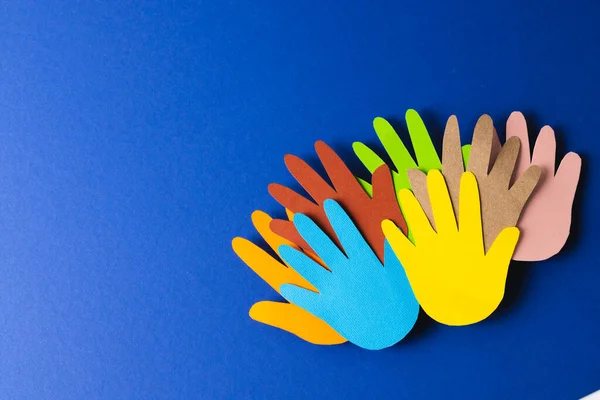 Close up of paper cut out of multi coloured hands with copy space on blue background. Humanitarian, people, help and human concept.
