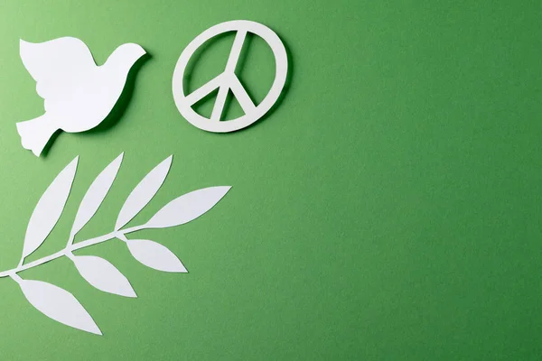 Close up of white dove and peace sign with leaves and copy space on green background. Peace and anti war movement concept.