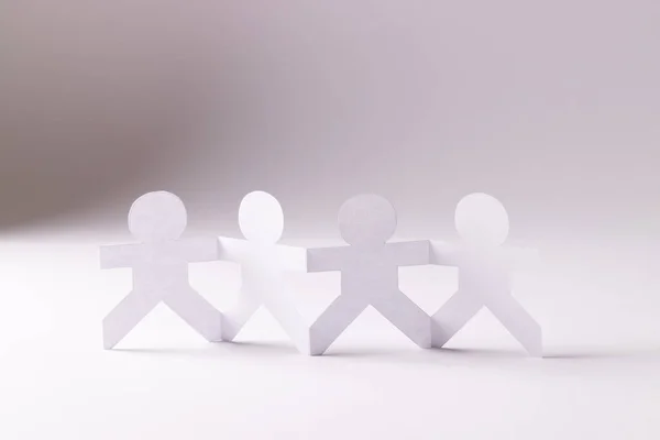 Close up of four paper cut out people figures holding hands with copy space on white background. Humanitarian, people, help and human concept.