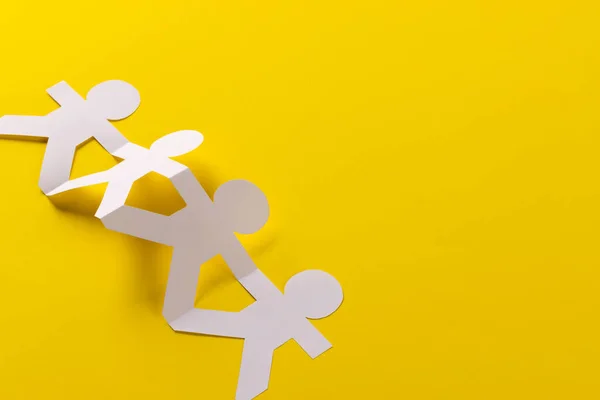 Close up of four paper cut out people figures holding hands with copy space on yellow background. Humanitarian, people, help and human concept.