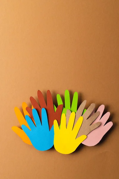 Close up of paper cut out of multi coloured hands with copy space on brown background. Humanitarian, people, help and human concept.