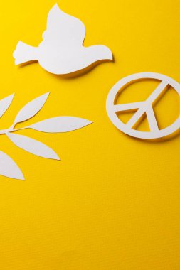 Beyaz barış işaretinin yüksek açılı görüntüsü, beyaz güvercin ve sarı arka planda kopya alanı olan yaprak. Barış ve savaş karşıtı hareket kavramı.