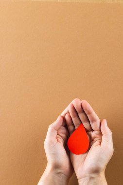 Kahverengi arka planda kan damlalarını kopyalayan beyaz kadının elleri. Kan bağışı, ilaç ve sağlık hizmetleri.