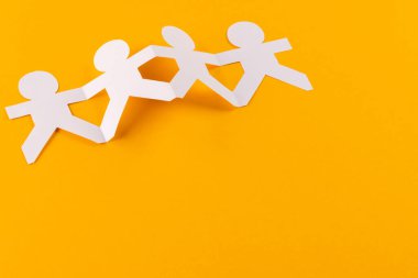 Turuncu arka planda fotokopi alanıyla el ele tutuşan dört kağıt kesimini kapatın. İnsani yardım, insanlar, yardım ve insan kavramı.