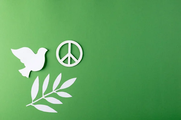 Close up of white dove and peace sign with leaves and copy space on green background. Peace and anti war movement concept.