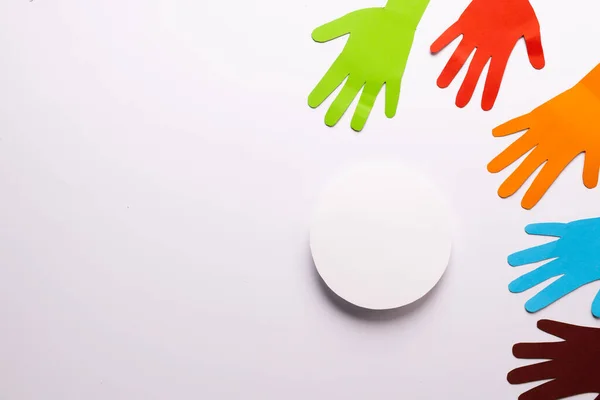 Paper cut out of multi coloured hands and white circle with copy space on white background. Humanitarian aid, people, help and human concept.
