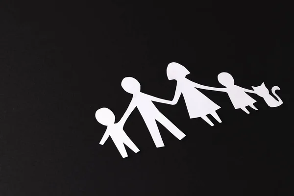 White paper cut out of family with two children and cat and copy space on black background. Humanitarian aid, people, help and human concept.