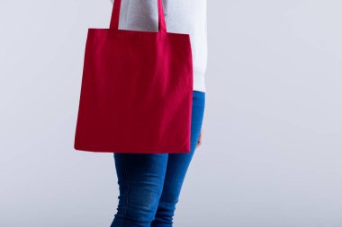 Beyaz kadın elinde gri arkaplanda kopya alanı olan kırmızı bir çanta tutuyor. Çantalar ve moda konsepti.