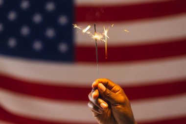 Amerika Birleşik Devletleri 'nin maytap ve bayrağını elinde tutan melez bir adamın eli. Amerikan vatanseverliği, bağımsızlık günü ve gelenek kavramı.