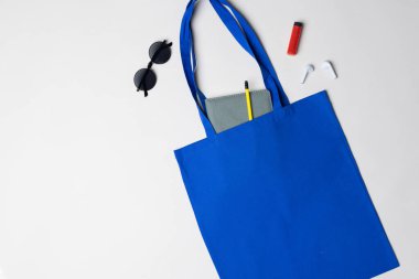 Not defteri, güneş gözlüğü, kulaklık ve çakmak içeren mavi tuval görüntüsü, kopyalama alanı. Çantalar ve moda konsepti.