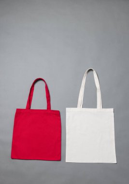 Gri arkaplanda kopya alanı olan beyaz ve kırmızı tuval çantalarını kapatın. Çantalar ve moda konsepti.