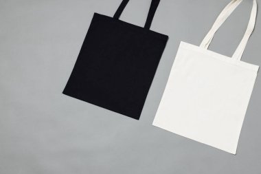 Gri arkaplan üzerinde fotokopi alanı olan siyah beyaz tuval çantaların yüksek açılı görüntüsü. Çantalar ve moda konsepti.