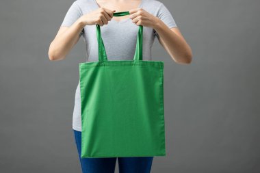 Beyaz kadın elinde gri arkaplanda fotokopi alanı olan yeşil bir çanta tutuyor. Çantalar ve moda konsepti.