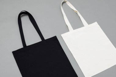 Gri arkaplan üzerinde fotokopi alanı olan siyah beyaz tuval çantaların yüksek açılı görüntüsü. Çantalar ve moda konsepti.