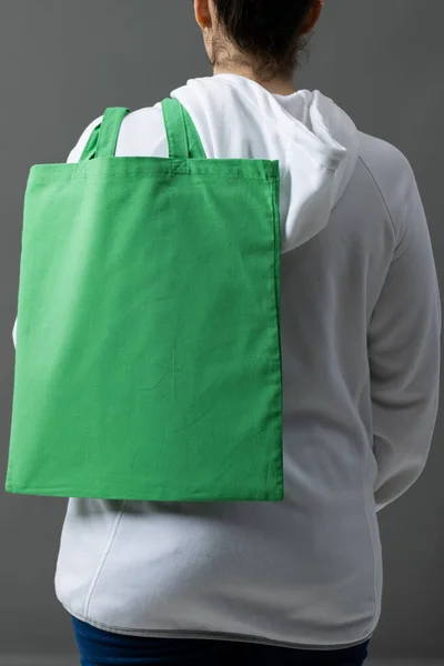 Caucasian woman holding over the shoulder green canvas bag with copy space on grey background. Bags and fashion concept.