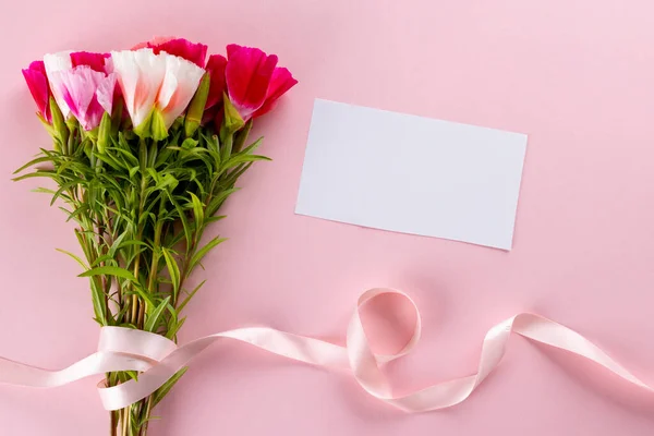 Image of pink and white flowers with ribbon and card with copy space on pink background. Mothers day, nature and spring concept.