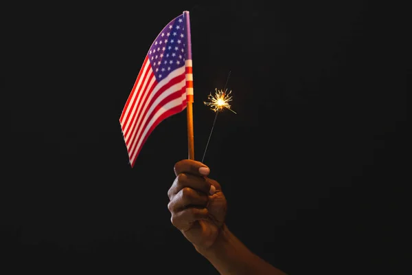 Hand of biracial man holding flag of united states of america and sparkler with copy space. American patriotism, independence day and tradition concept.