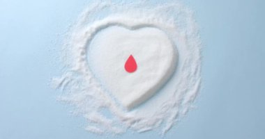 Kan damlasını kalp şeklindeki şekerin üzerine yakın çekim mavi arka planda, yavaş çekimde. Diyet, kan şekeri, diyabet ve kalp sağlığı farkındalığı.
