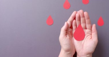 Beyaz kadının elleri kan damlasını tutuyor, gri arka planda fotokopi alanı var, yavaş çekim. Kan bağışı, ilaç ve sağlık hizmetleri.