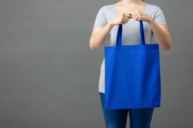 Beyaz kadın elinde gri arka planda kopya alanı olan mavi bir çanta tutuyor. Çantalar ve moda konsepti.