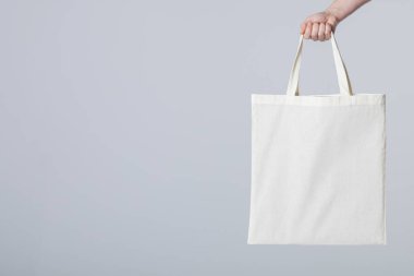 Beyaz bez çanta tutan beyaz bir kadının eli. Arka planda fotokopi alanı var. Çantalar ve moda konsepti.