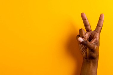 Çift ırklı bir adamın, sarı arka planda fotokopi alanı olan barış işareti göstermesinin yakın çekimi. Barış ve savaş karşıtı hareket kavramı.