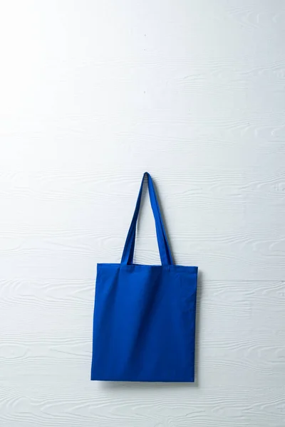 Close up of hanging blue canvas bag with copy space on white background. Eco friendly shopping bags and fashion concept.