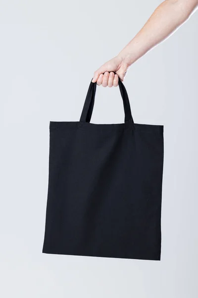 グレーの背景にコピースペースの黒いキャンバスバッグを持つ白人女性の手 バッグとファッションのコンセプト — ストック写真