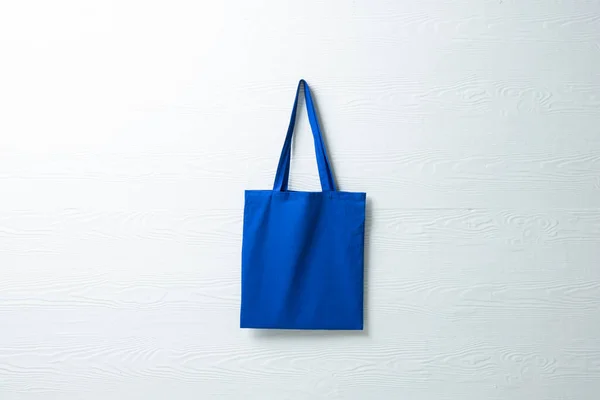 Close up of hanging blue canvas bag with copy space on blue background. Eco friendly shopping bags and fashion concept.
