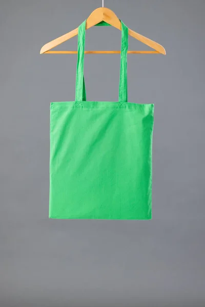 Close up of green canvas bag hanging on wooden clothes hanger with copy space on grey background. Eco friendly shopping bags and fashion concept.