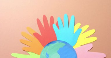 Ellerinizi kapayın ve kahverengi arkaplanda fotokopi alanı olan renkli kağıtlardan yapılmış küreyle birleştirin. Topluluk, küresel, insanlar ve sanat.