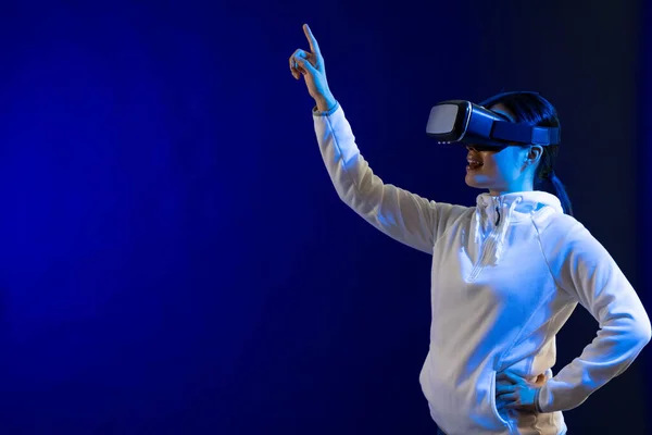 Happy asian woman using vr headset in studio with blue light with copy space. Virtual reality and digital interface technology.