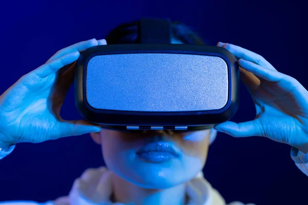 Portrait of asian woman holding vr headset in studio with blue light. Virtual reality and digital interface technology.