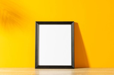 Sarı duvar ve yaprakların gölgesinde kopya alanı olan siyah boş çerçeve. Çerçeve şablonu, iç tasarım ve dekorasyonu düzenle.