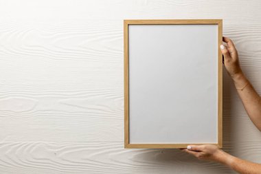 Elleri tahta boş çerçeve ve beyaz duvara karşı fotokopi alanı tutuyor. Çerçeve şablonu, iç tasarım ve dekorasyonu düzenle.