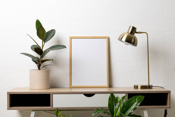 Wood empty frame with copy space, lamp and plants in pots on table against white wall. Mock up frame template, interior design and decoration.