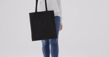 Beyaz kapüşonlu beyaz kadın beyaz arka planda siyah çanta tutuyor. Kopya alanı, ağır çekim. Moda, tasarım, kıyafetler ve kumaş.