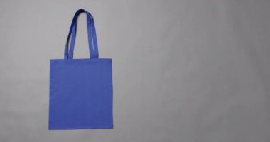 Gri arkaplandaki mavi çantayı fotokopi alanıyla kapat, yavaş çekimde. Moda, tasarım ve kumaş.