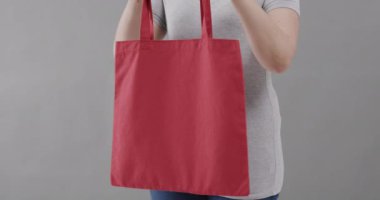 Beyaz tişört giyen beyaz kadın gri arka planda kırmızı çanta tutuyor, fotokopi alanı, ağır çekim. Moda, tasarım, kıyafetler ve kumaş.