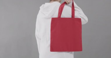 Beyaz kapüşonlu beyaz kadın gri arka planda kırmızı çanta tutuyor. Kopya alanı, ağır çekim. Moda, tasarım, kıyafetler ve kumaş.